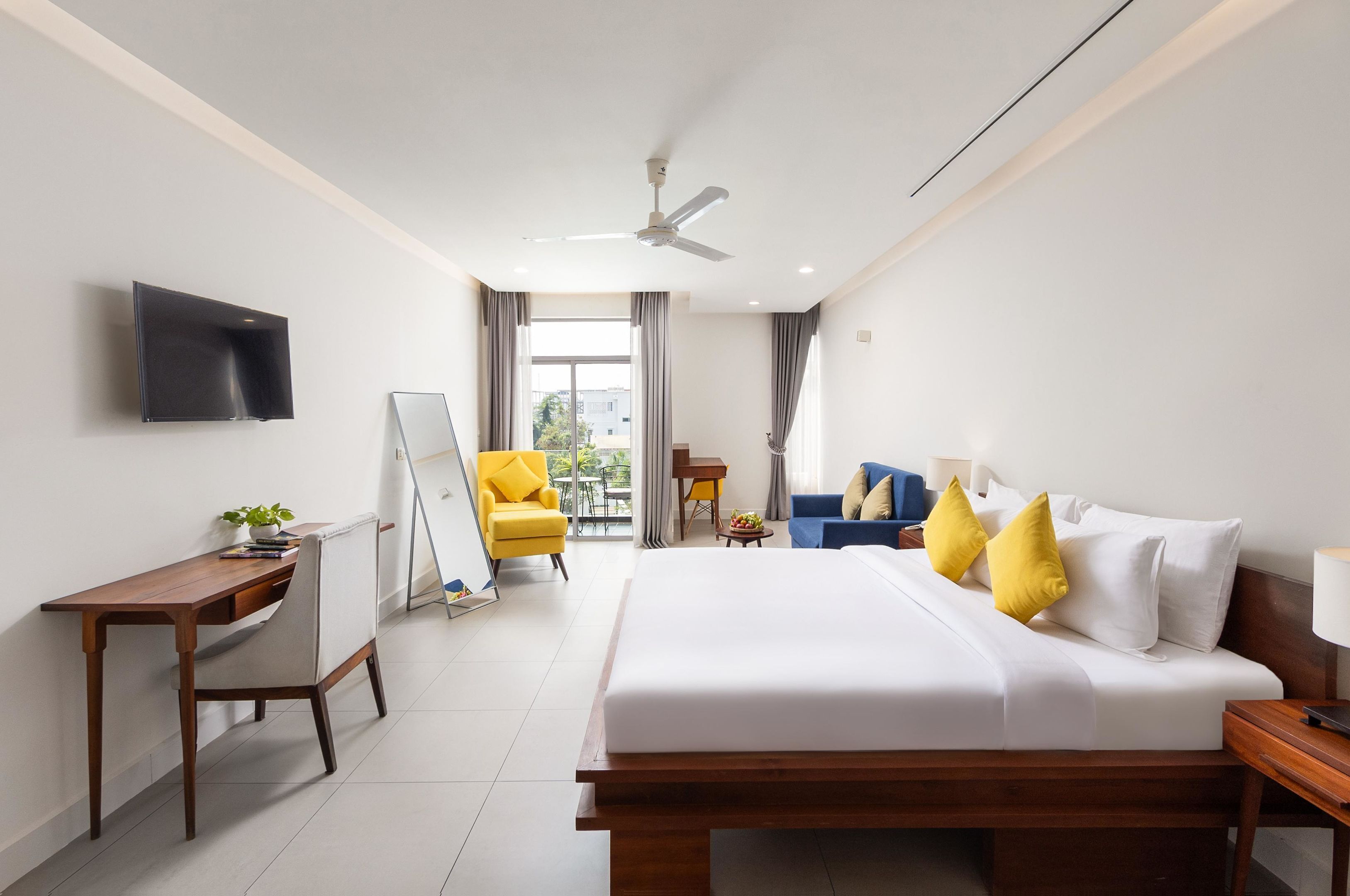 Hotelkamer met een bed, bureau, stoel, televisie en balkonuitzicht.