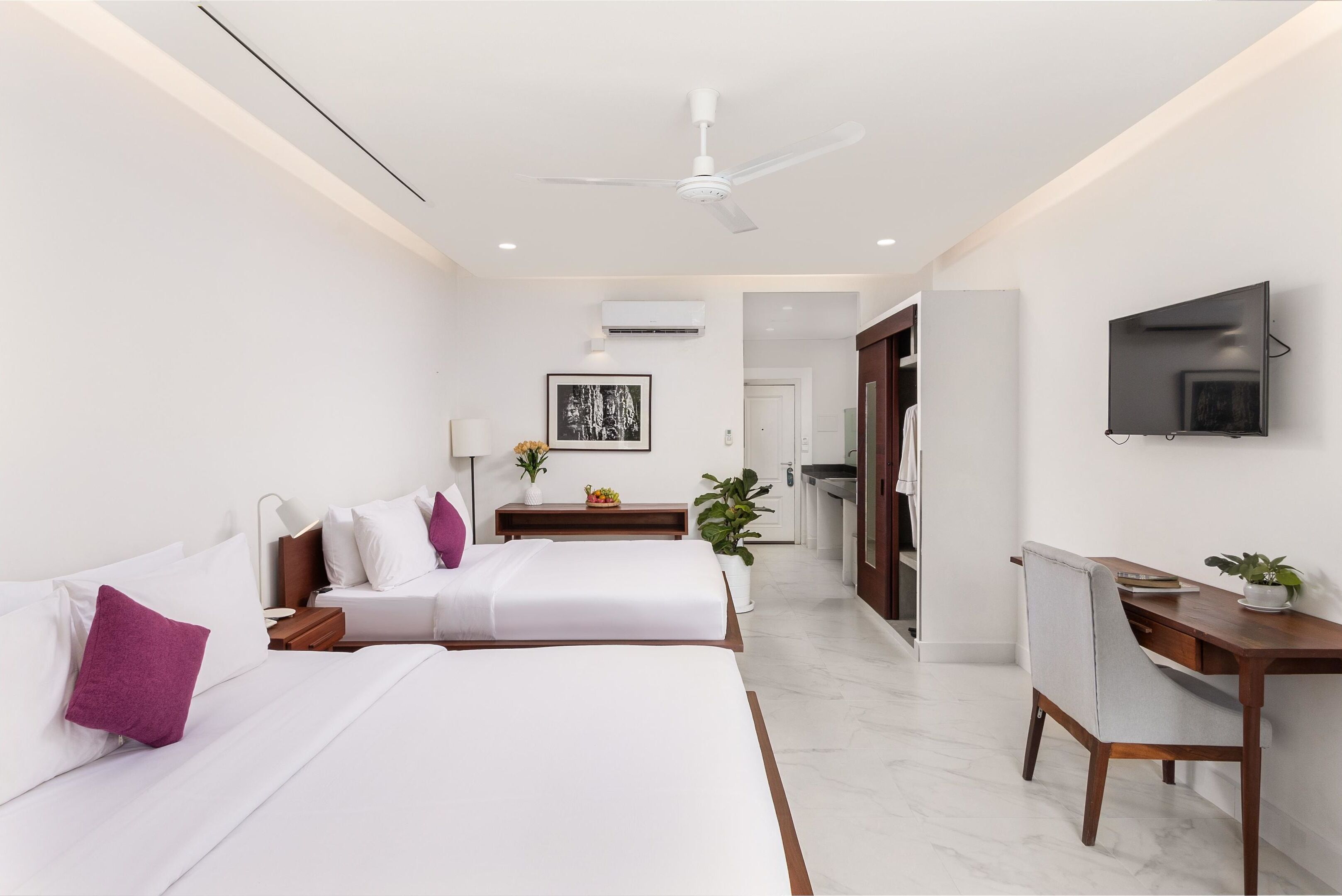A modern hotel room with two beds, a desk, a chair, a TV, and an air conditioning unit.