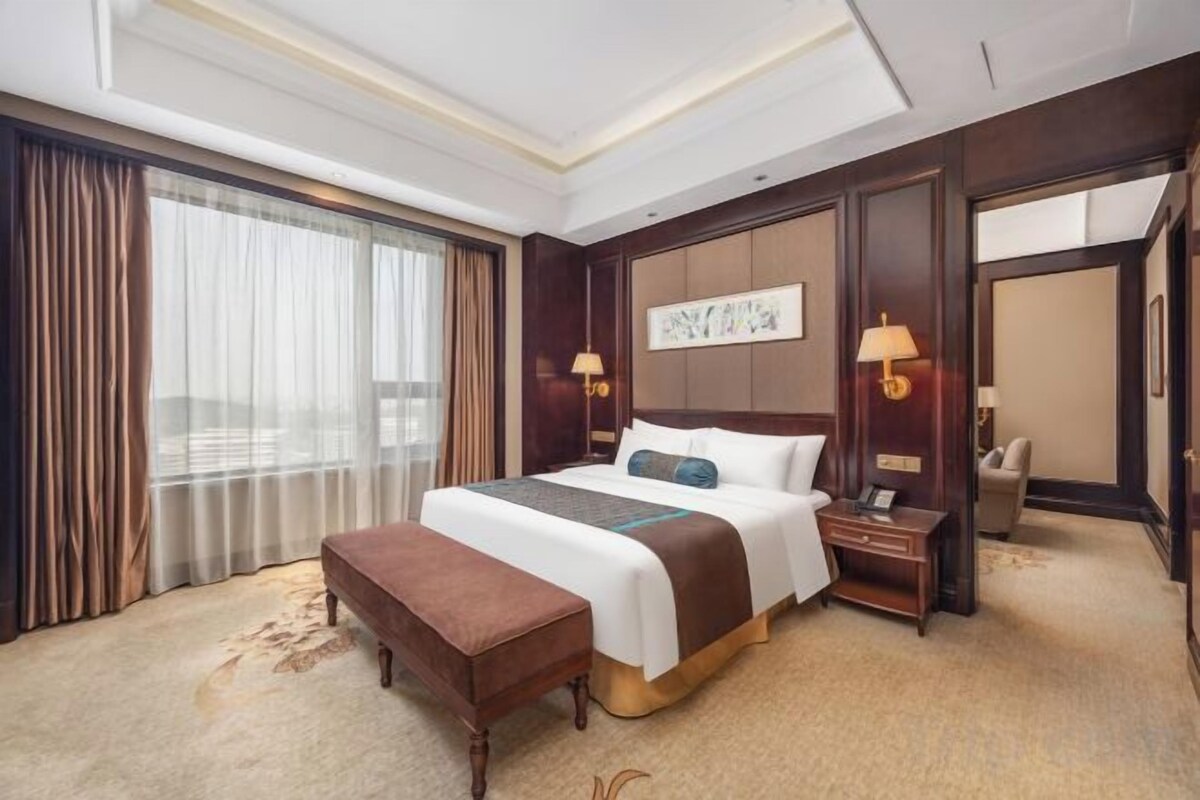 A hotel room with a large bed, a desk, a chair, and a view of the city.