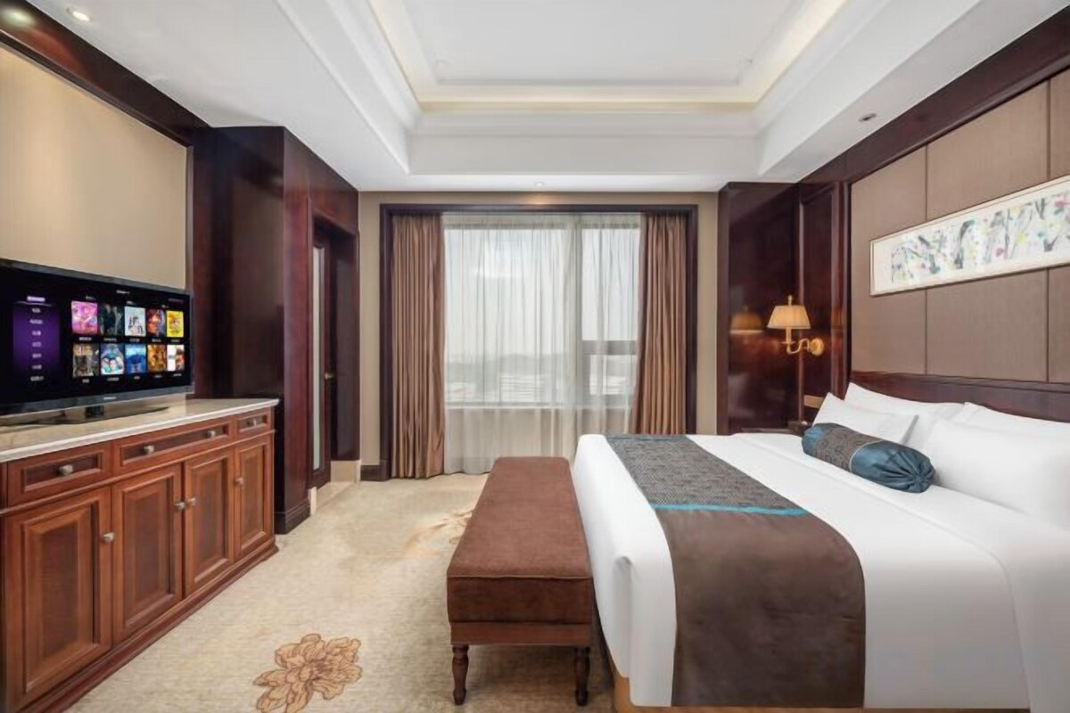Een hotelkamer met een bed, een televisie, een bureau en een groot raam met gordijnen.