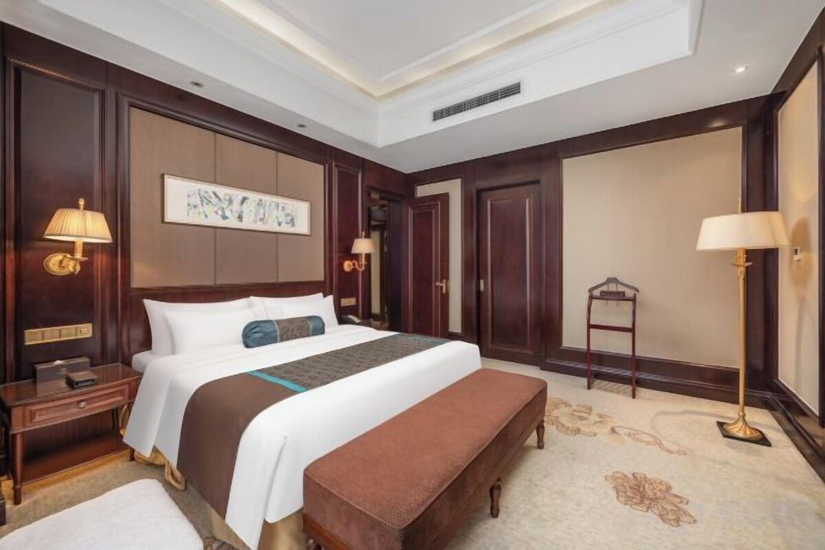 Habitación de hotel con una cama grande, mesitas de noche, un banco, un escritorio y una silla.
