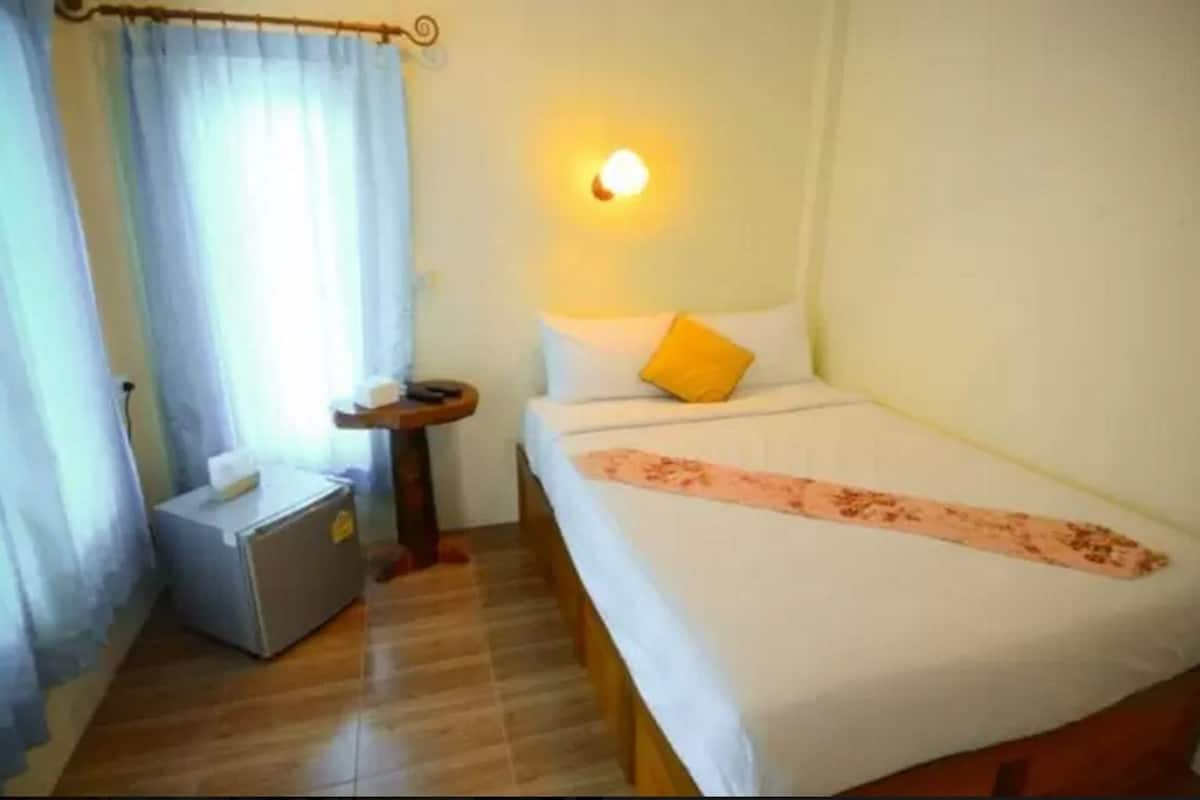 Una habitación pequeña y ordenada, con cama, mesita de noche, lámpara y un armario pequeño.