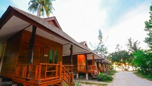 A row of wooden cabins with balconies, surrounded by lush greenery and a dirt path leading to a beach. - Baanchaylay Resort (Khanom)