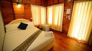 A wooden-paneled room with a large bed, a nightstand, and curtains. - Baanchaylay Resort (Khanom)