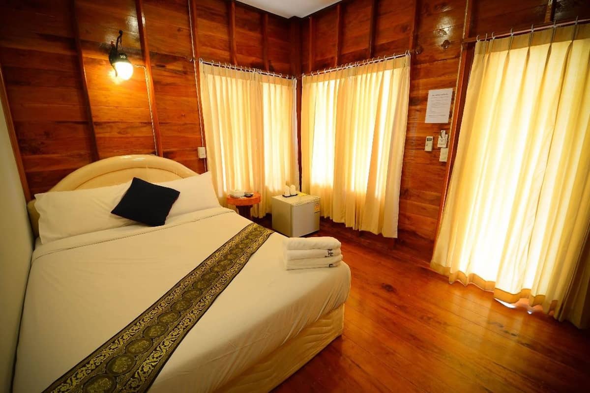 Una habitación con paneles de madera, una cama grande, una mesita de noche y cortinas.
