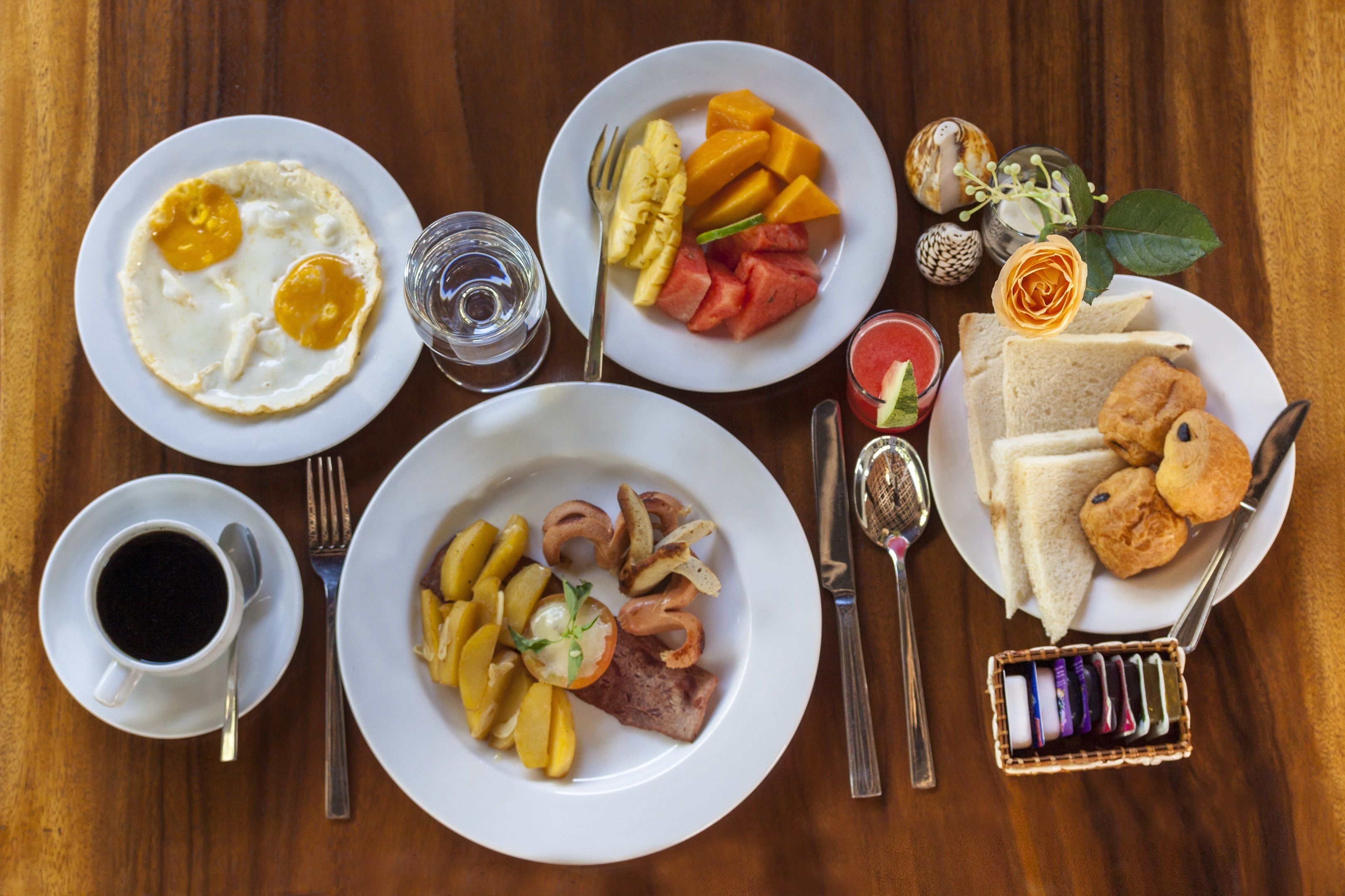 A breakfast setting with plates of eggs, fruit, toast, and pastries.