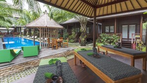 A pool area with lounge chairs and a gazebo, surrounded by wooden structures and tropical plants.