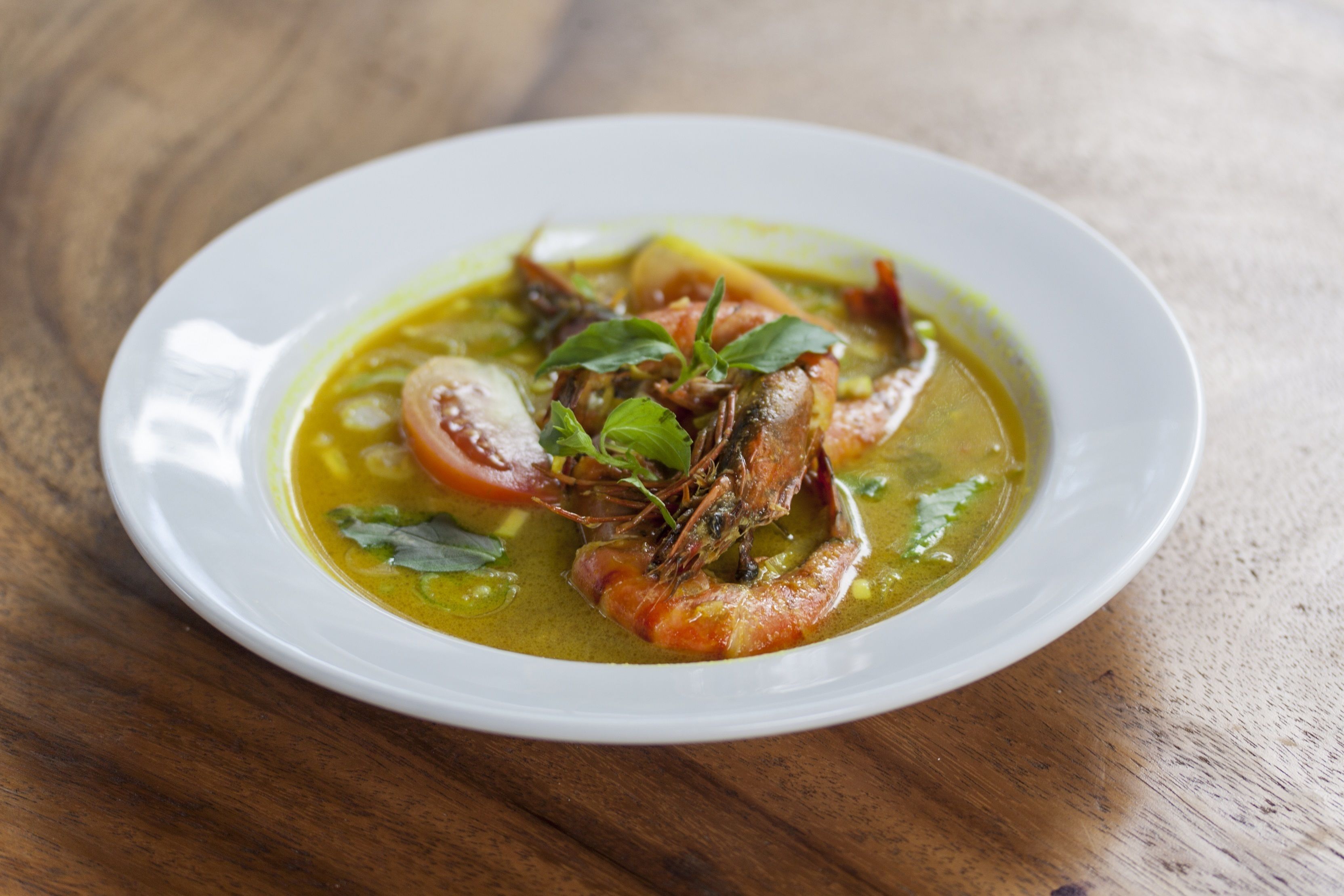 Ein weißer Teller mit einem Fischgericht, möglicherweise eine Suppe oder ein Eintopf, auf einem Holztisch.