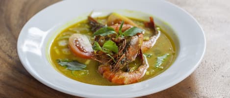Un plato blanco con un plato de mariscos, posiblemente sopa o guiso, sobre una mesa de madera.