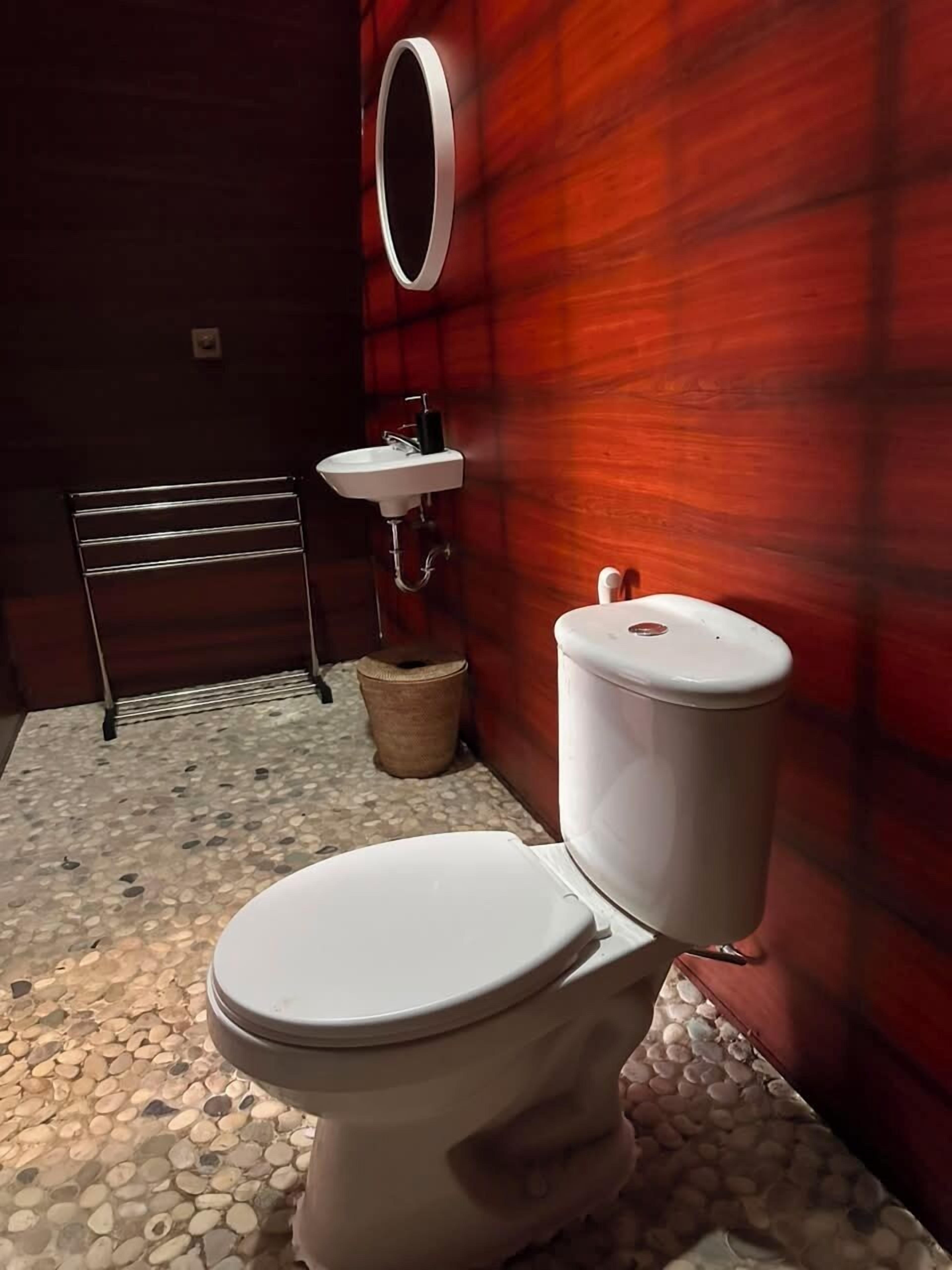 Un baño con inodoro blanco, lavamanos, espejo y toallero.