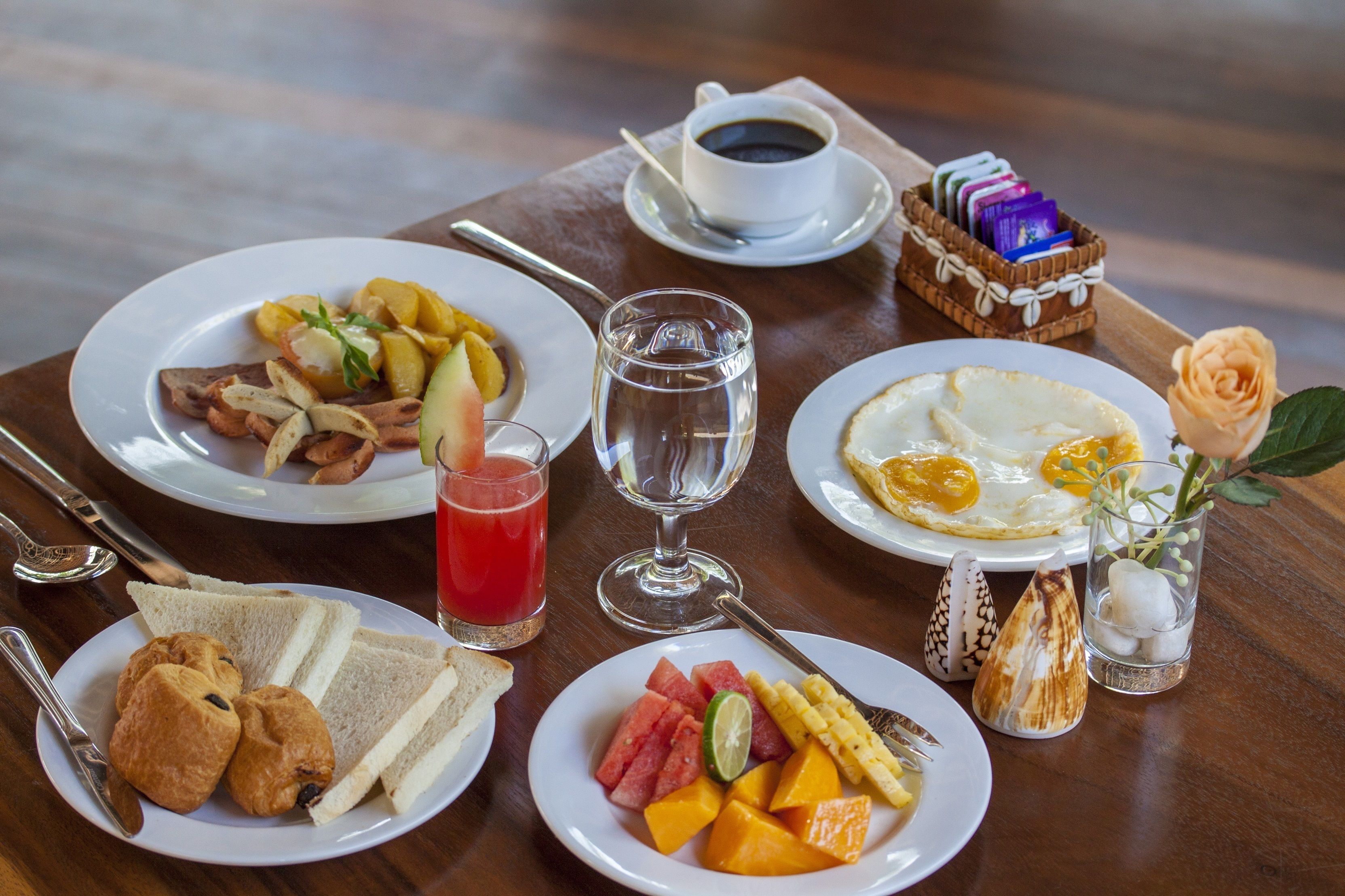 Desayuno con platos de comida, un vaso de jugo rojo, una taza de café y un objeto decorativo pequeño.