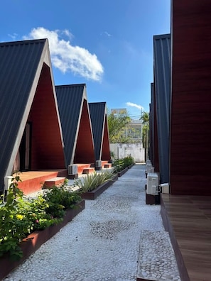 A row of modern, triangular-roofed structures with a gravel pathway and greenery in between.