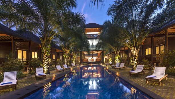 A pool area with lounge chairs, palm trees, and a building with a balcony.