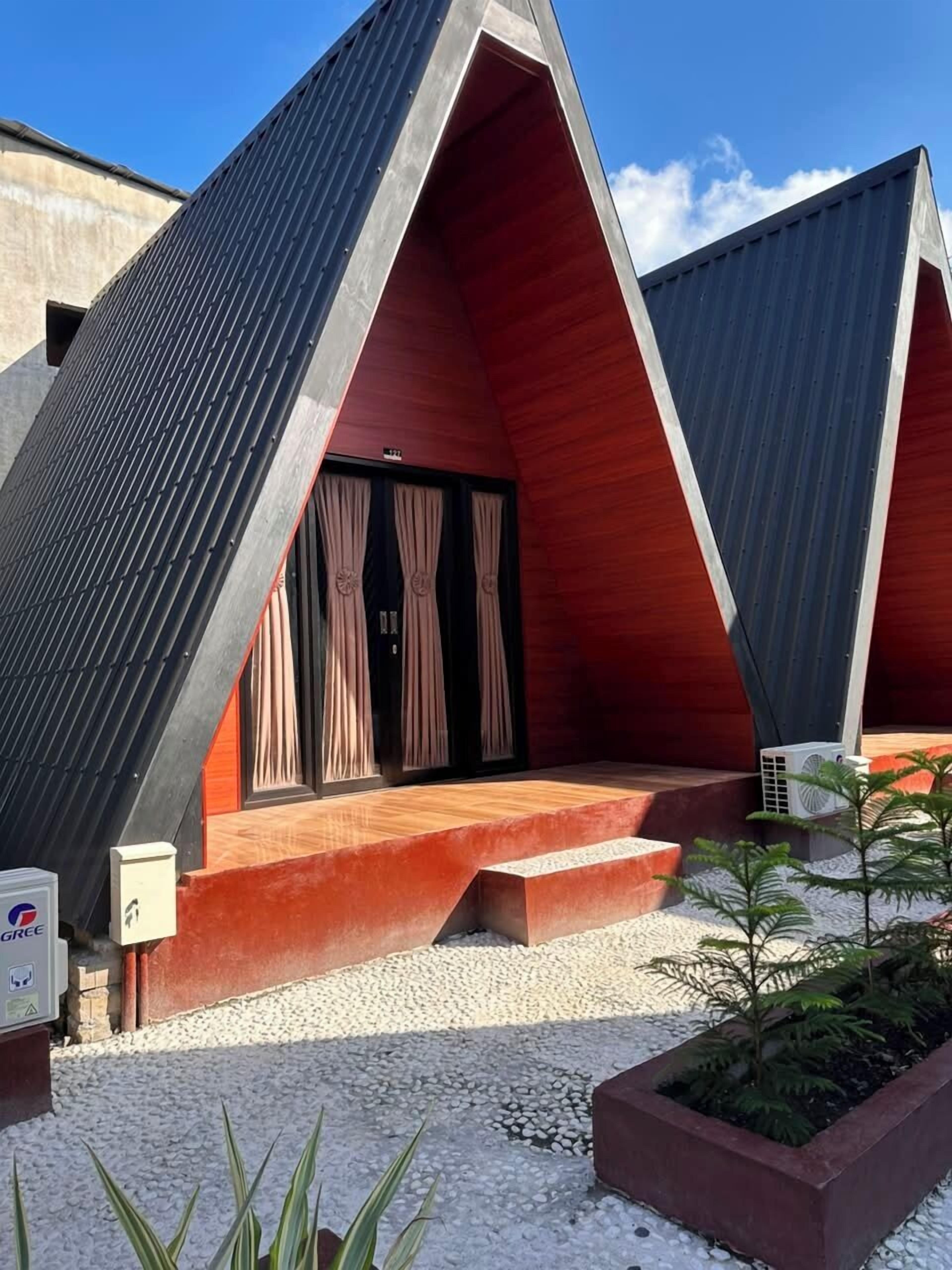 Un edificio moderno con techo triangular, un pequeño espacio de asientos al aire libre y suelo de grava.