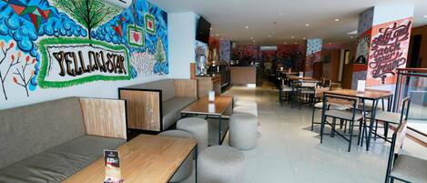 Un interior de restaurante moderno con un mural, disposición de mesas y una barra.