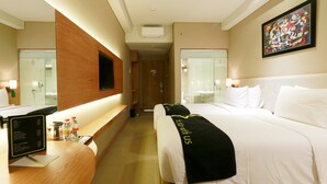 Quarto de hotel com uma cama, uma mesa com computador, um espelho e um quadro na parede.