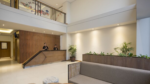 Um lobby moderno com balcão de recepção, escada, área de estar e plantas em vasos.