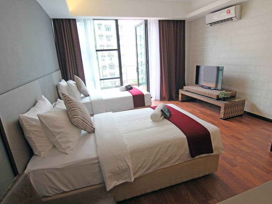 Quarto de hotel com duas camas, televisão e uma grande janela com cortinas.
