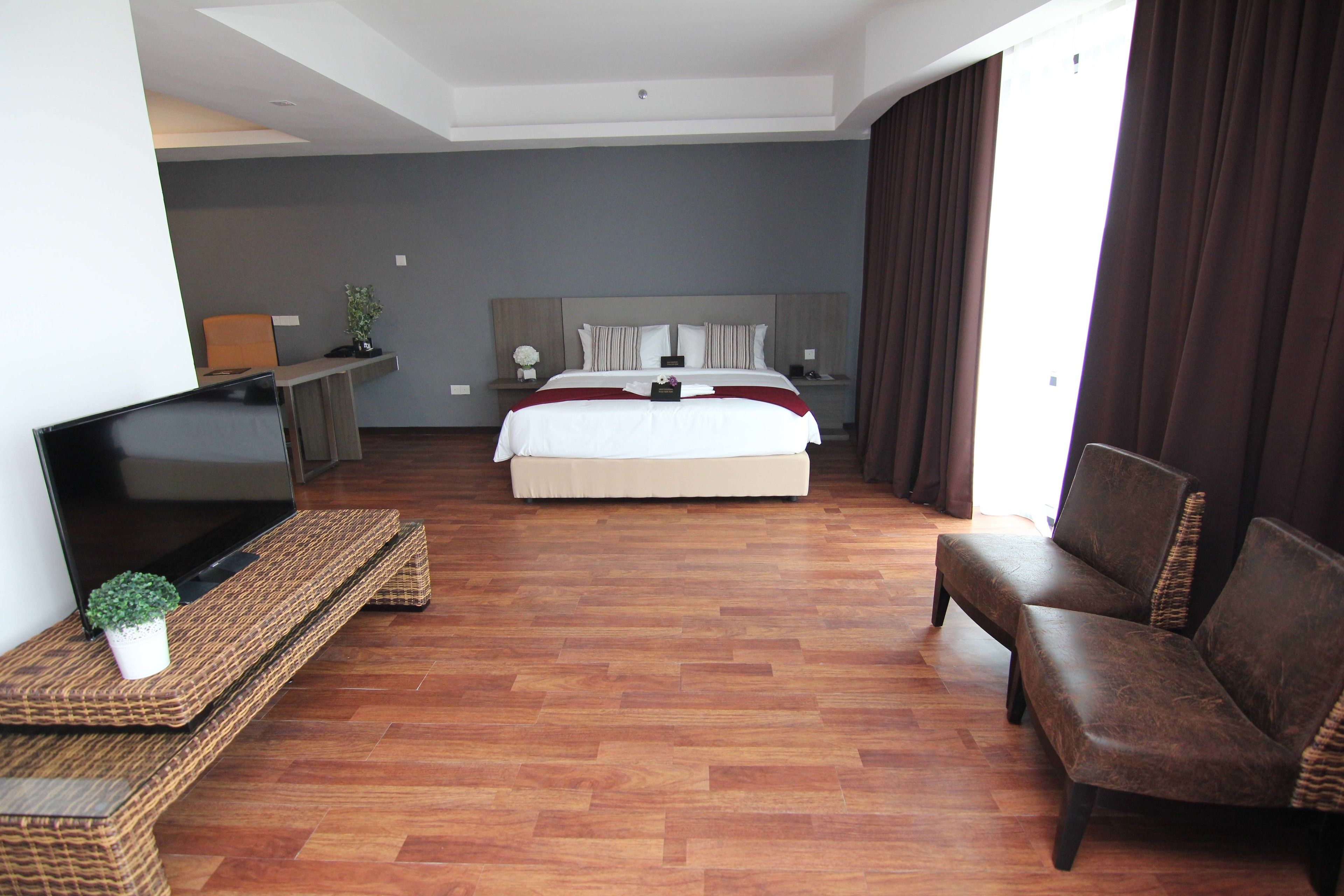 A hotel room with a large bed, a TV on a stand, a sofa, and a desk with a plant.
