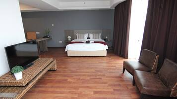 A hotel room with a large bed, a TV on a stand, a sofa, and a desk with a plant.