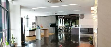 A modern hotel lobby with a polished black floor, a reception desk, and a seating area with a sofa.