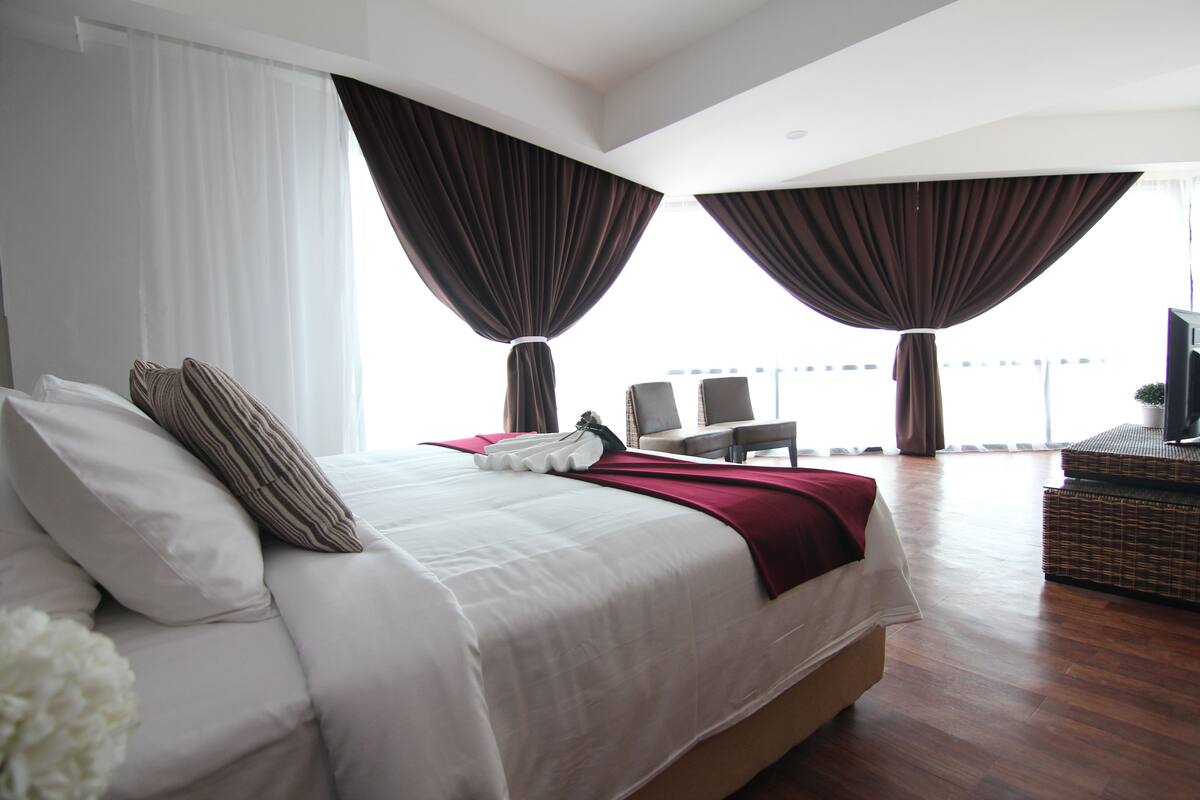 Una habitación de hotel moderna con una cama grande, dos sillones, una mesita y un televisor.