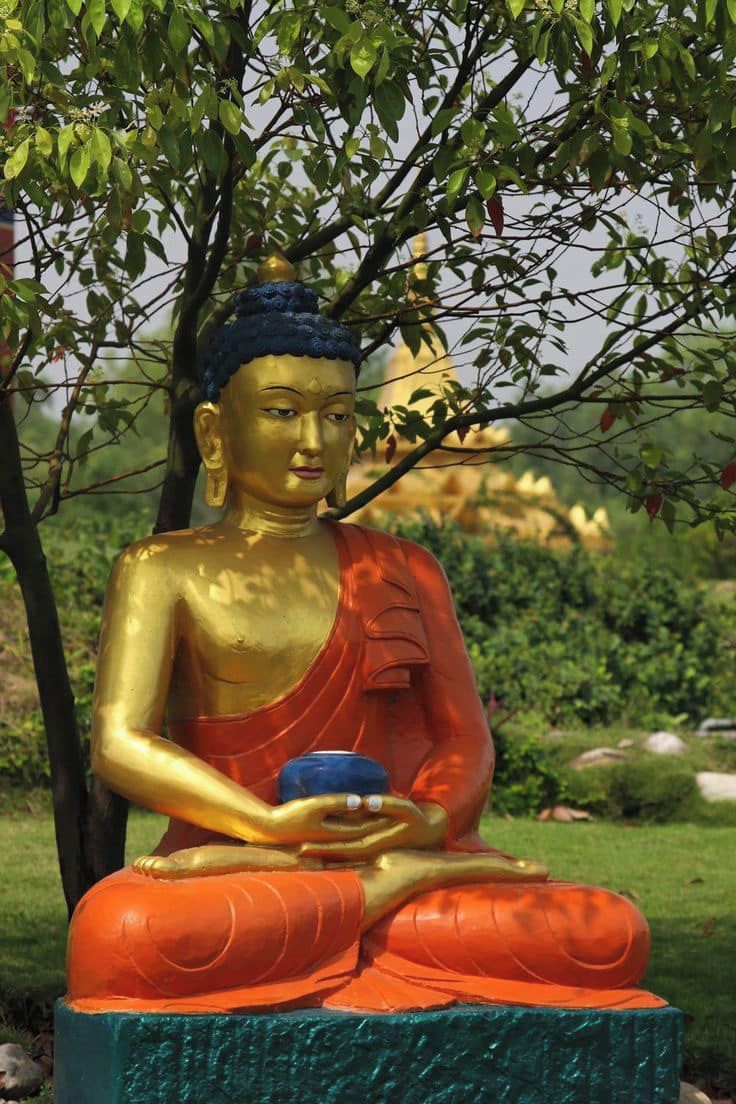 A statue of a seated figure in a meditative pose, surrounded by greenery.