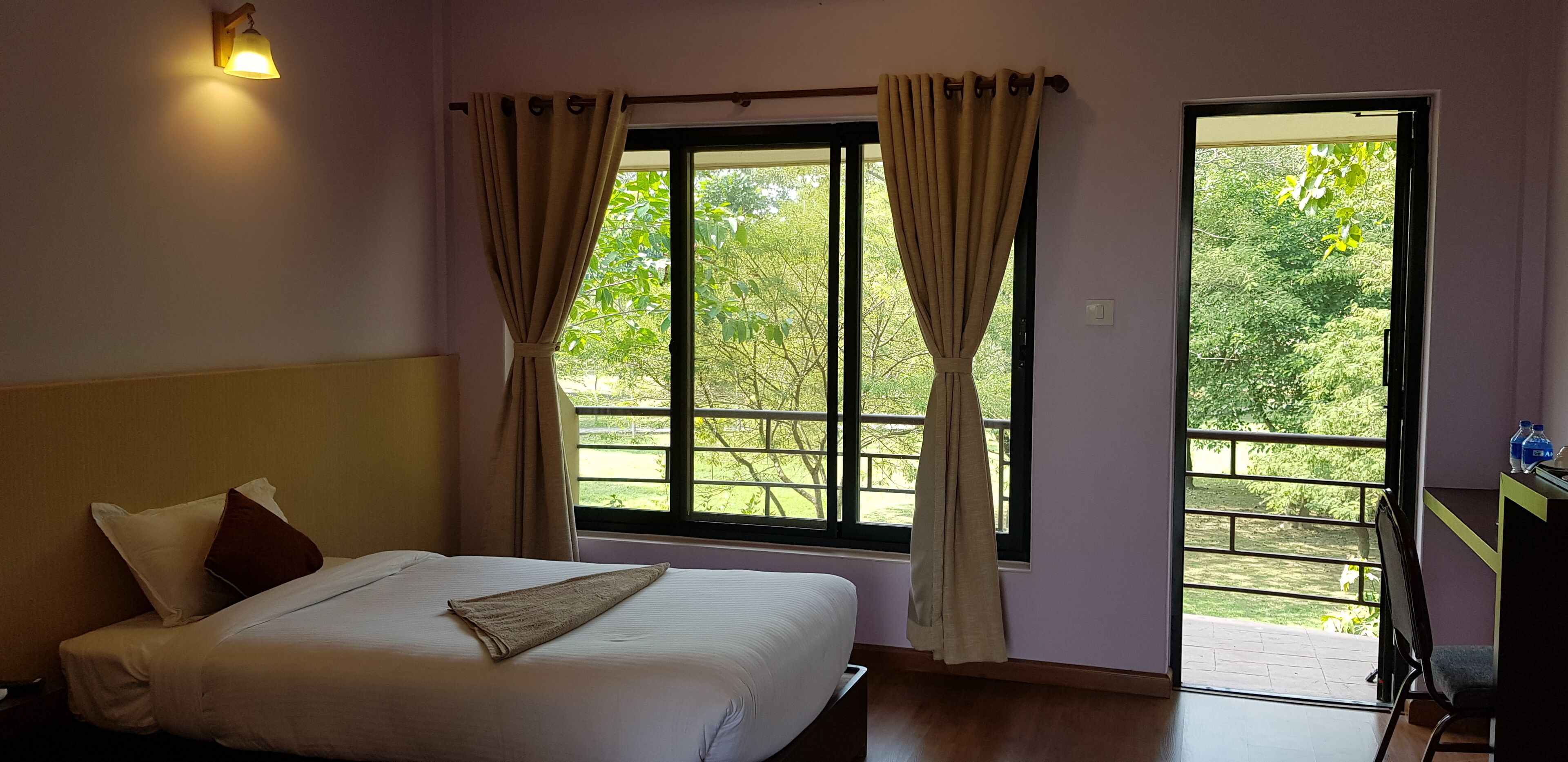 A bedroom with a bed, curtains, a window, and a view of greenery outside.