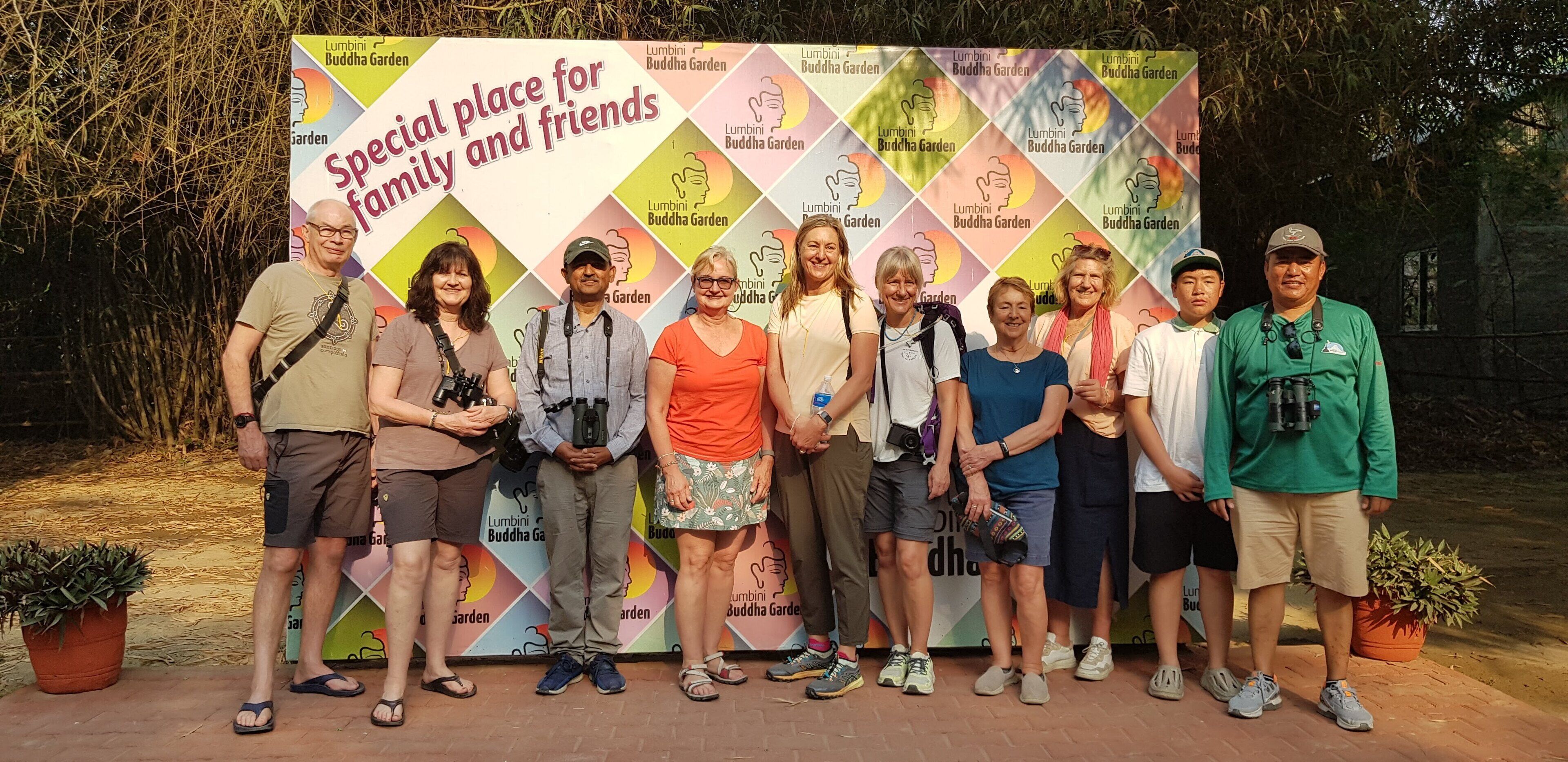 A group of people standing in front of a colorful backdrop with the text "Special place for family and friends" and "Lumbini Buddha Garden".