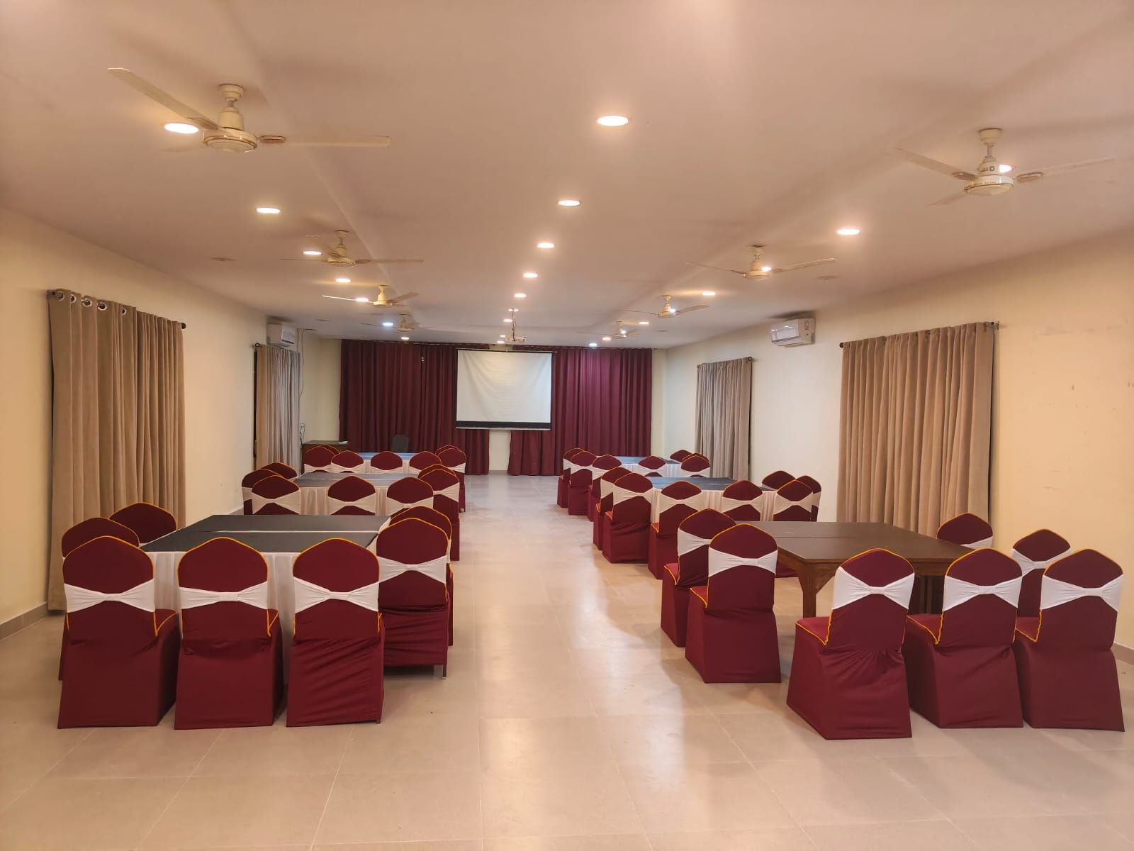 A conference room with tables and chairs, ceiling fans, and a projector screen.