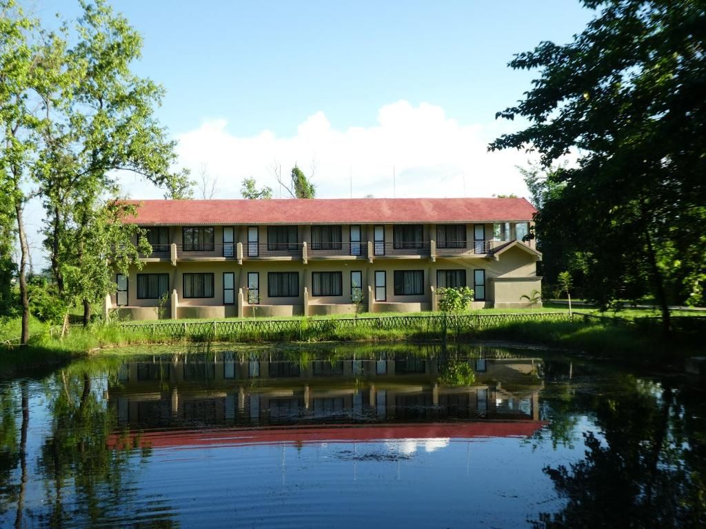 Un bâtiment à deux étages, surmonté d’un toit rouge, dont le reflet se mire dans les eaux calmes.
