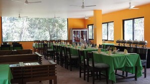 Comedor con mesas dispuestas para una comida, sillas, ventiladores de techo y ventanas amplias con vistas a árboles.