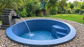 A circular hot tub with a water feature, surrounded by a pebble border, set in a landscaped garden. - Lumbini Buddha Garden Resort (Lumbini)