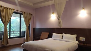 Habitación de hotel con una cama grande, una mesita de noche, una silla y un ventanal con cortinas.