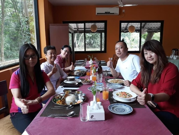 Un grupo de personas comiendo en una mesa con varios platos, una botella de zumo de naranja y un salero.