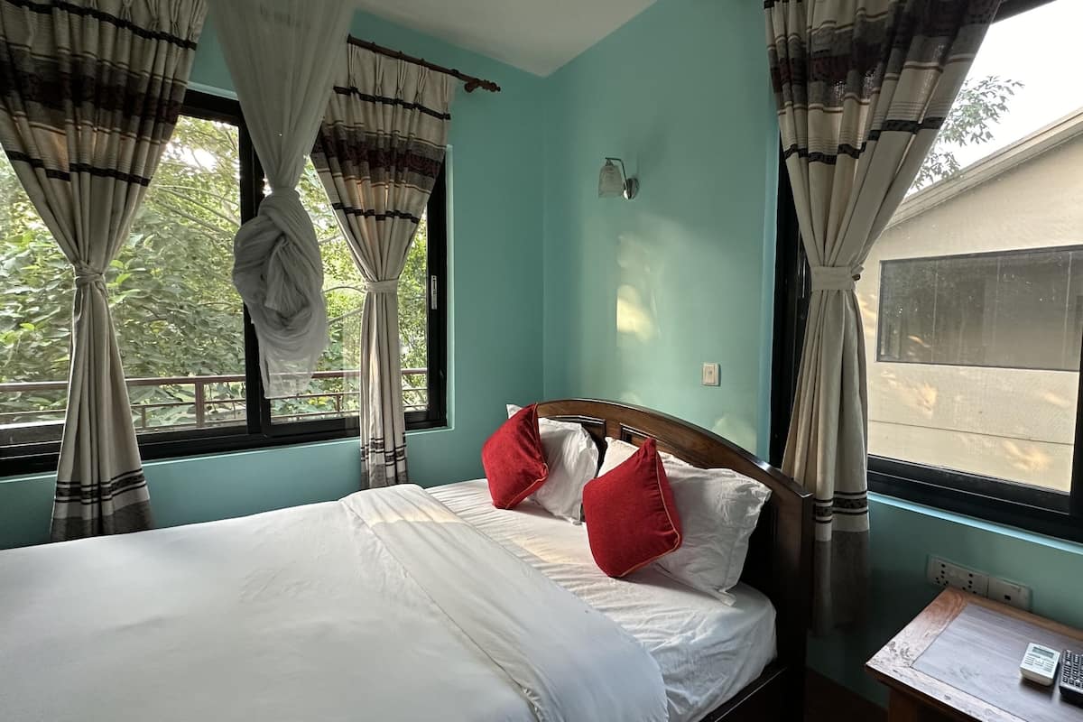 A room with a bed, a nightstand, a window with curtains, and a view of the outside.