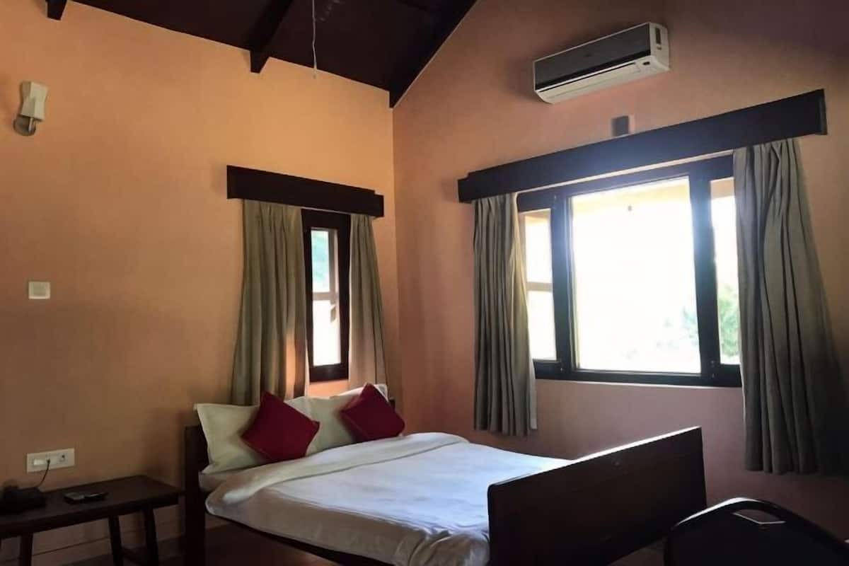 A bedroom with a bed, a bedside table, a chair, and a window with curtains.