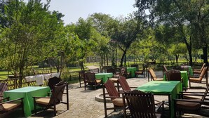 Un patio al aire libre con mesas y sillas de madera, rodeado de árboles y una cerca.