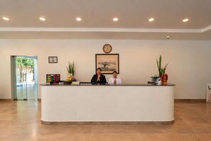 A reception desk with two staff members, a clock, and framed artwork on the wall. - Lumbini Buddha Garden Resort (Lumbini)