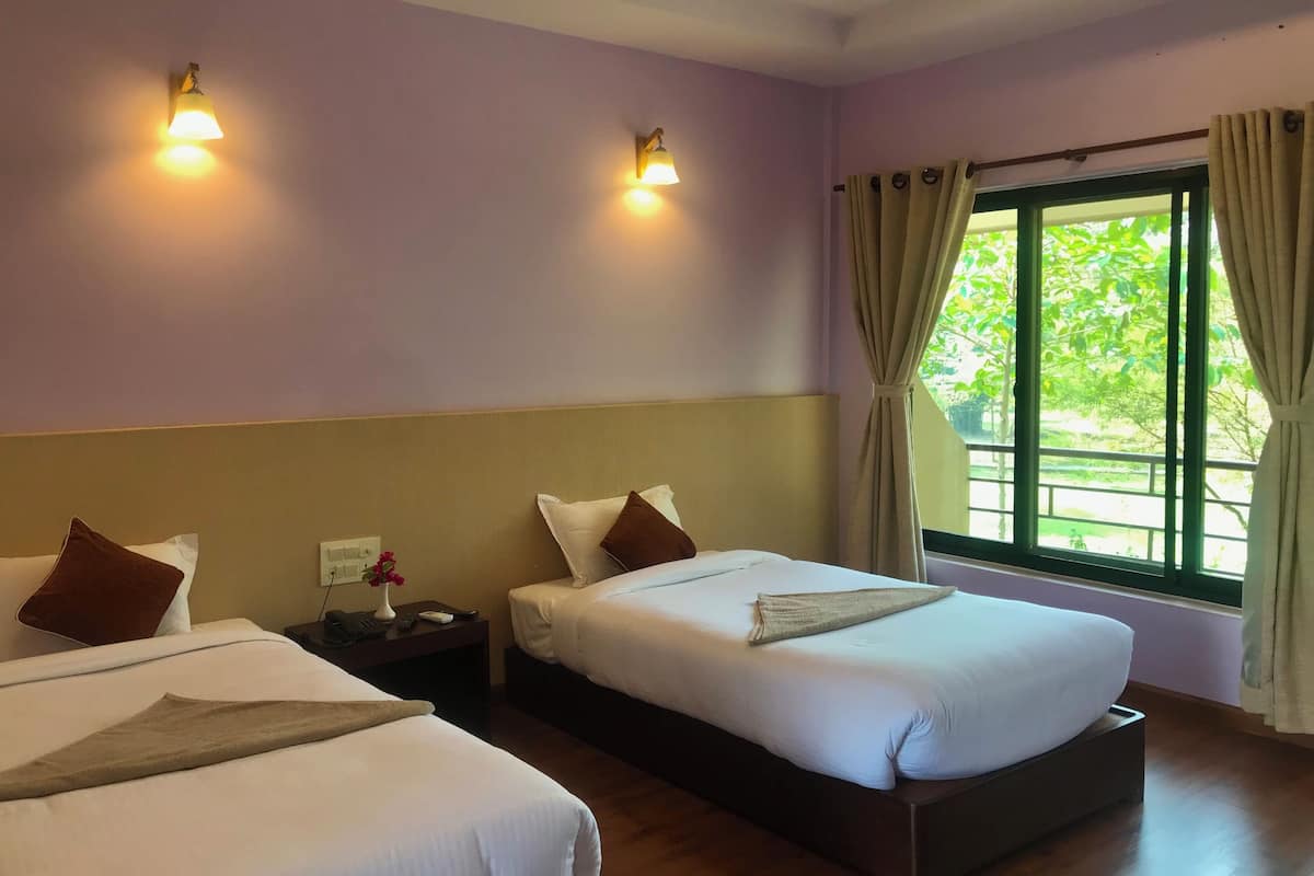 A hotel room with two beds, a nightstand with a vase of flowers, a window with curtains, and wall-mounted lights.