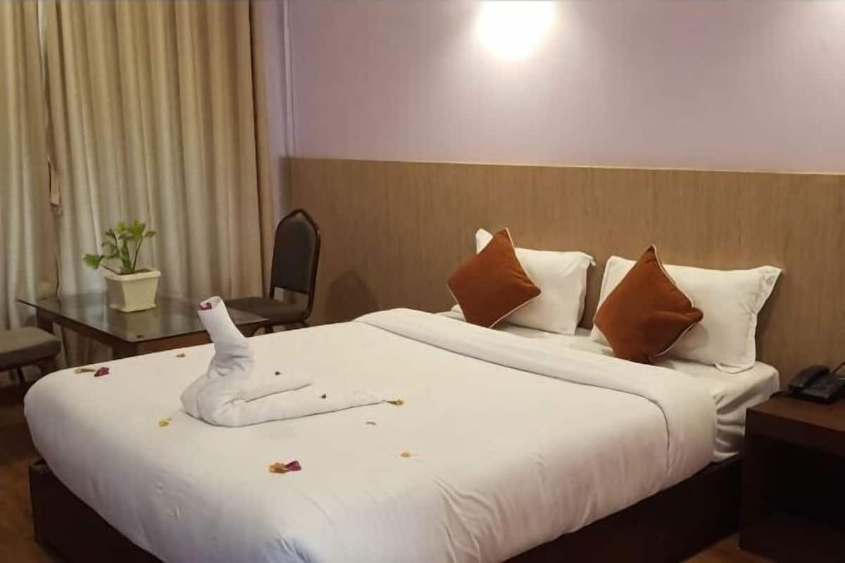 A hotel room with a bed, a desk, a chair, a potted plant, and a nightstand.