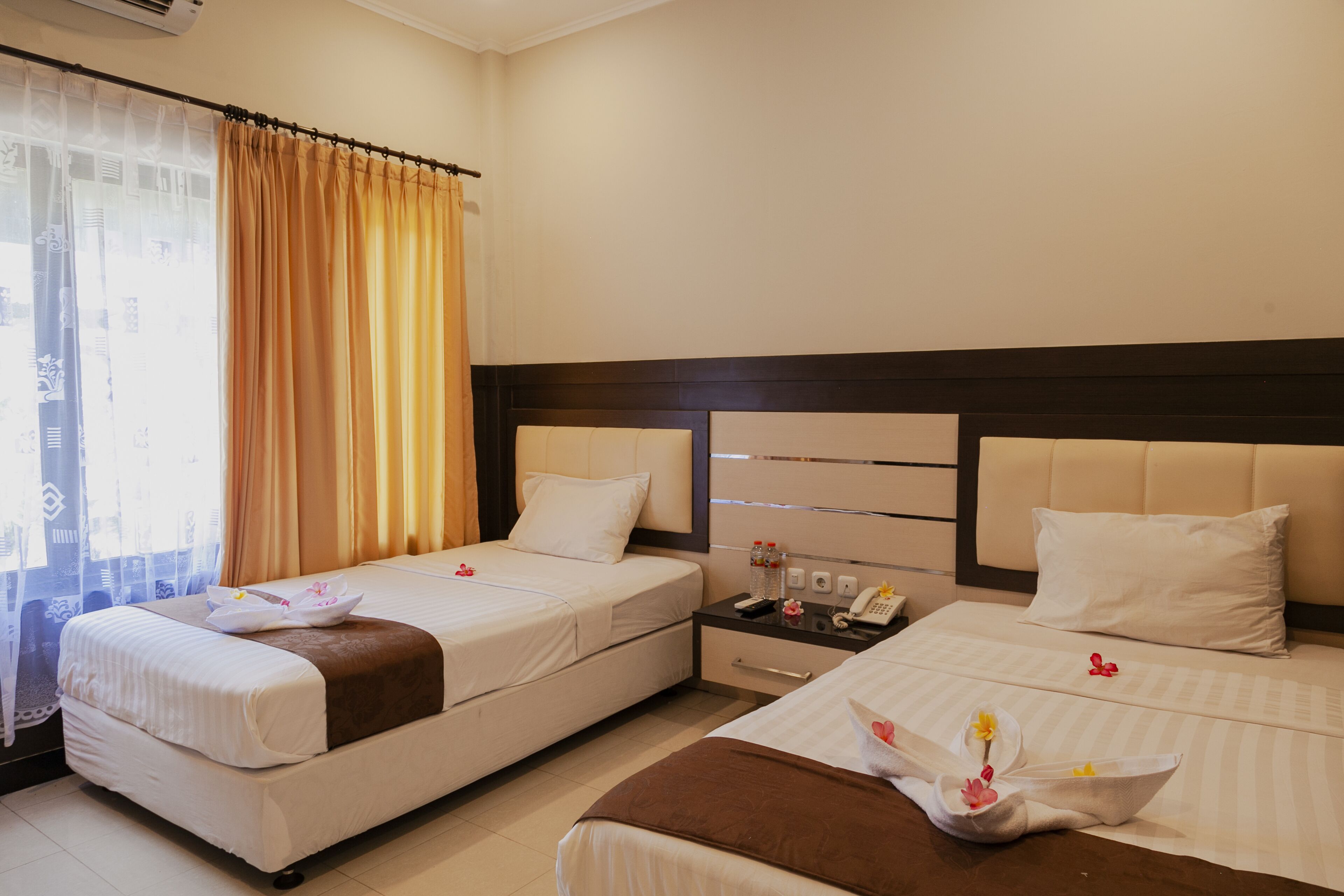 A hotel room with two beds, a nightstand, and a window with curtains.