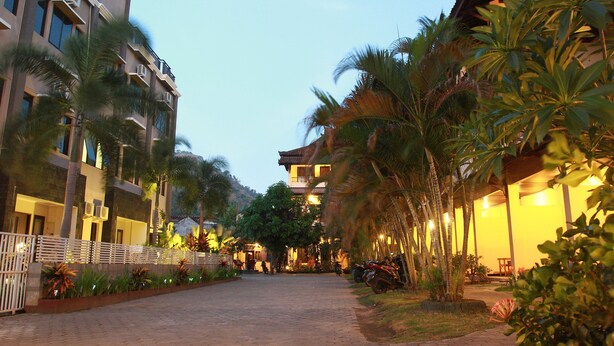 A hotel with a paved walkway, palm trees, and a building with balconies. - Puri Senggigi Hotel (Senggigi)