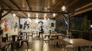 An indoor dining area with tables and chairs, a mural on the wall, and hanging lights. - Puri Senggigi Hotel (Senggigi)