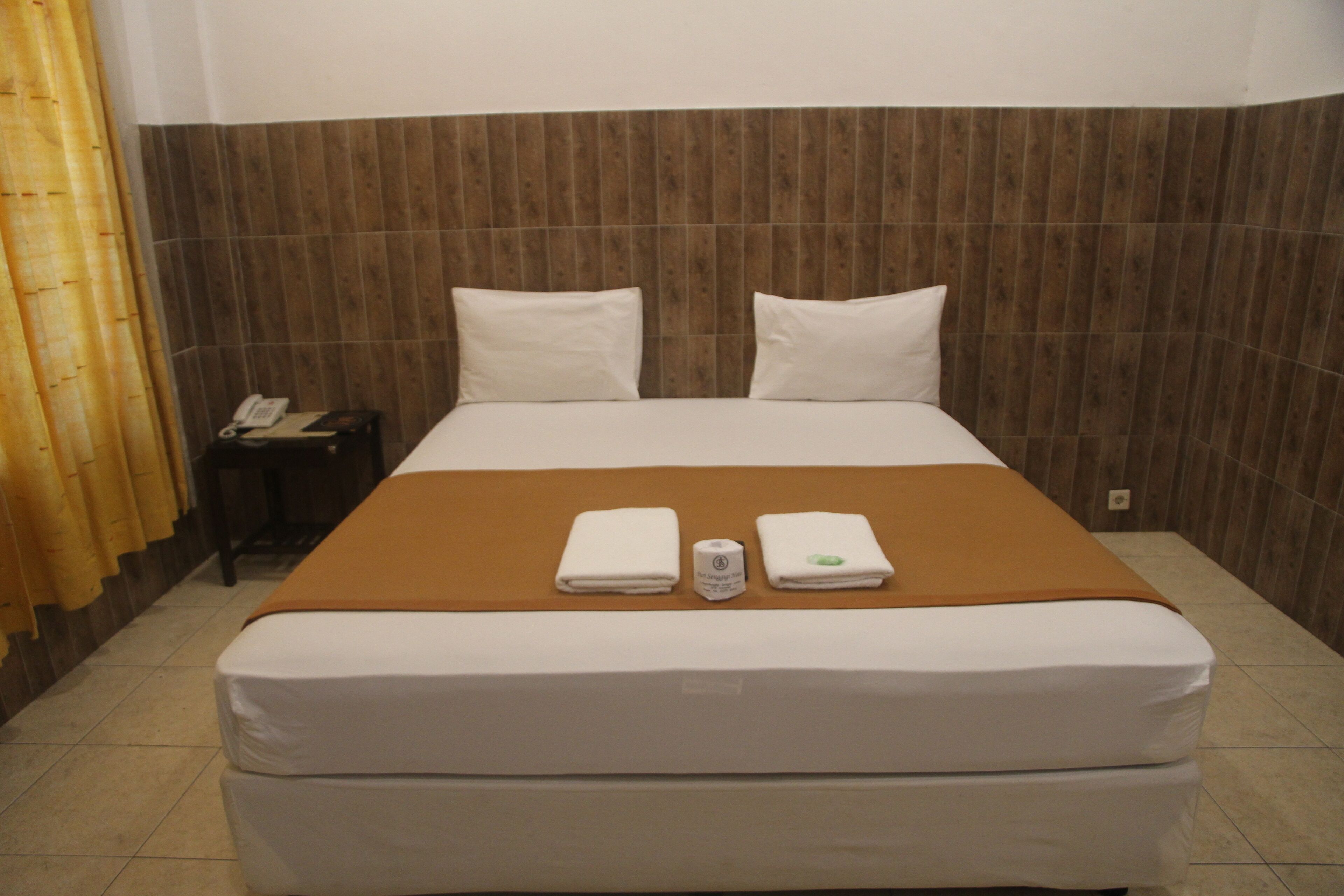 A hotel room with a large bed, two pillows, a brown blanket, and two folded towels.