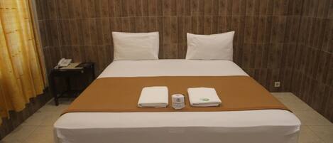 A hotel room with a large bed, two pillows, a brown blanket, and two folded towels.