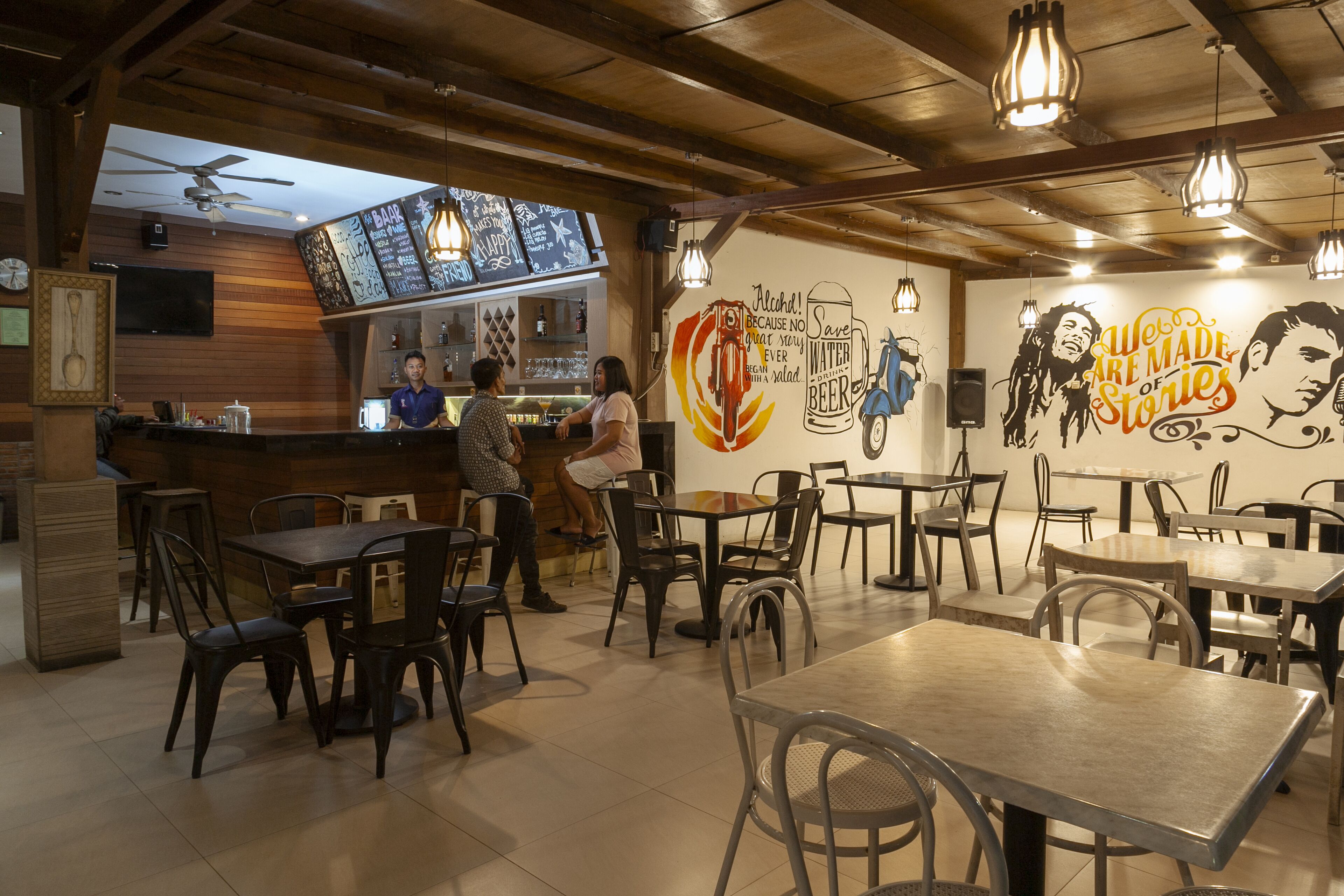 A restaurant interior with wooden beams, hanging light fixtures, and a bar area.