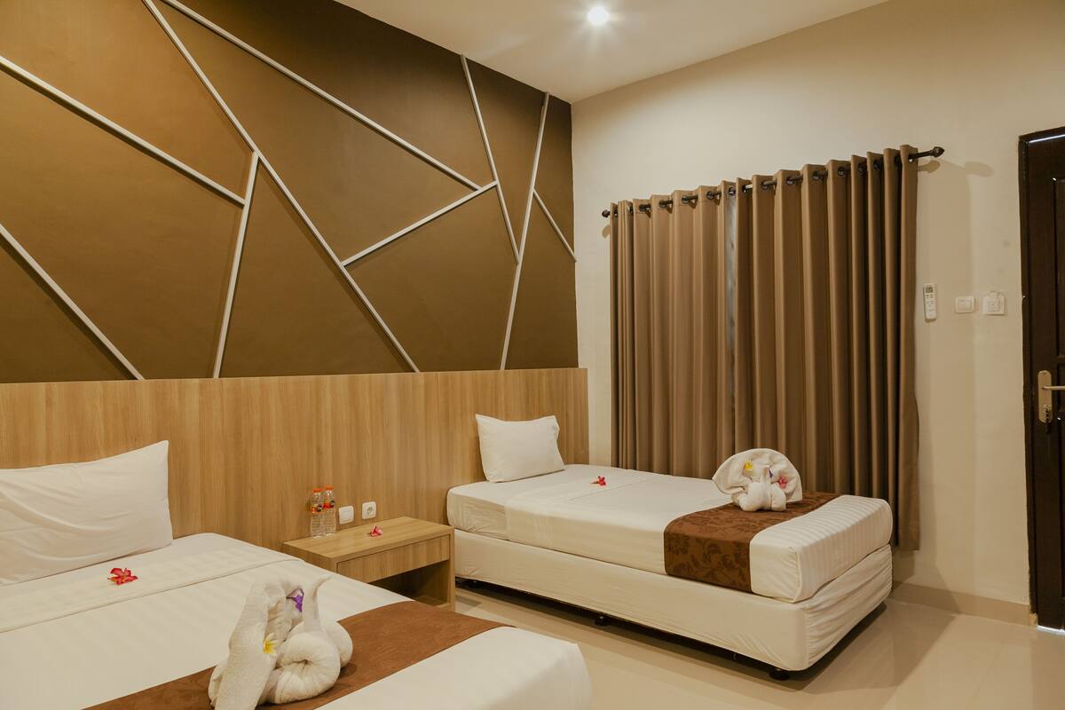 Une chambre d’hôtel avec deux lits, une tête de lit en bois, une table de chevet et une fenêtre avec des rideaux.