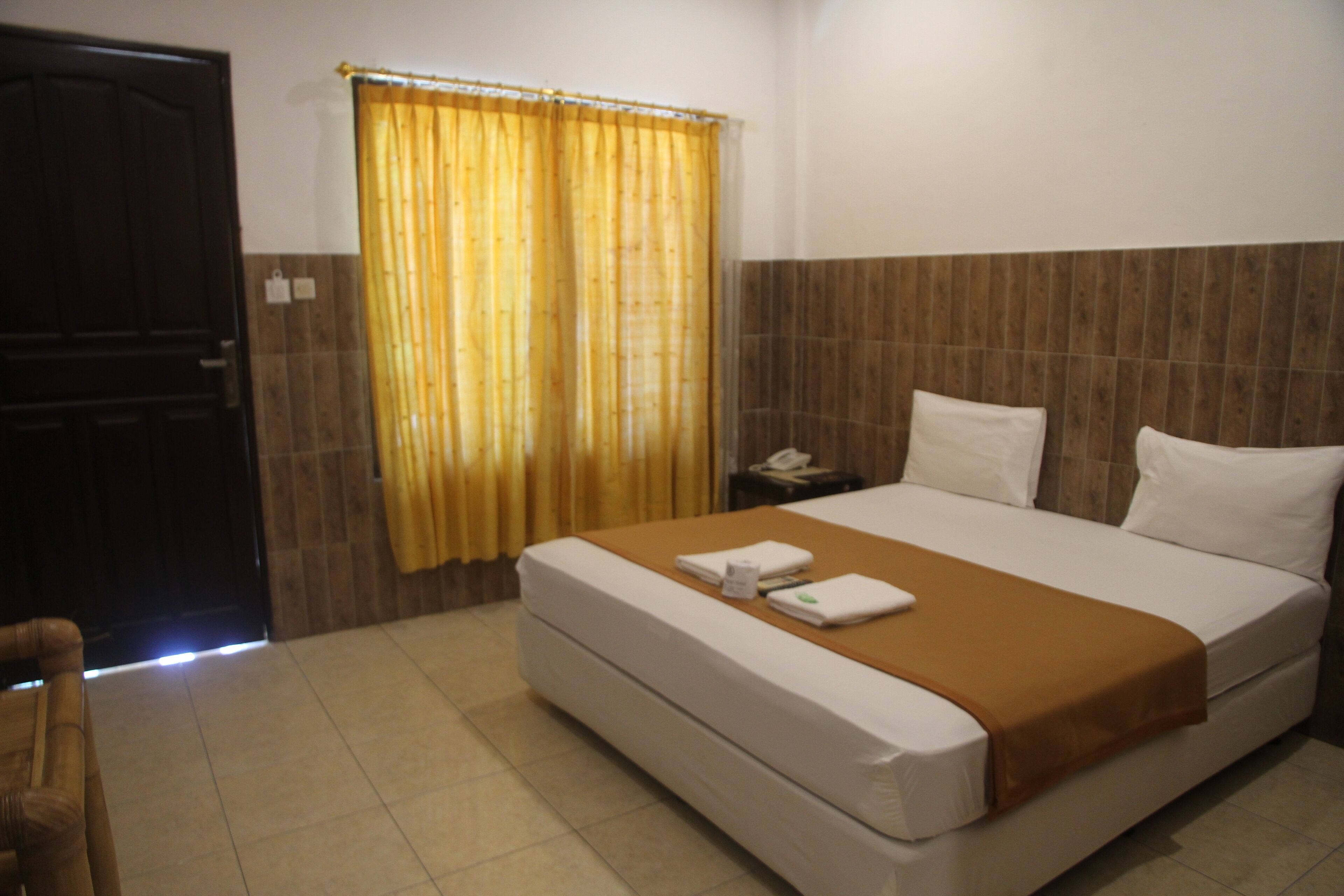 A hotel room with a bed, a nightstand, a telephone, and a curtain.