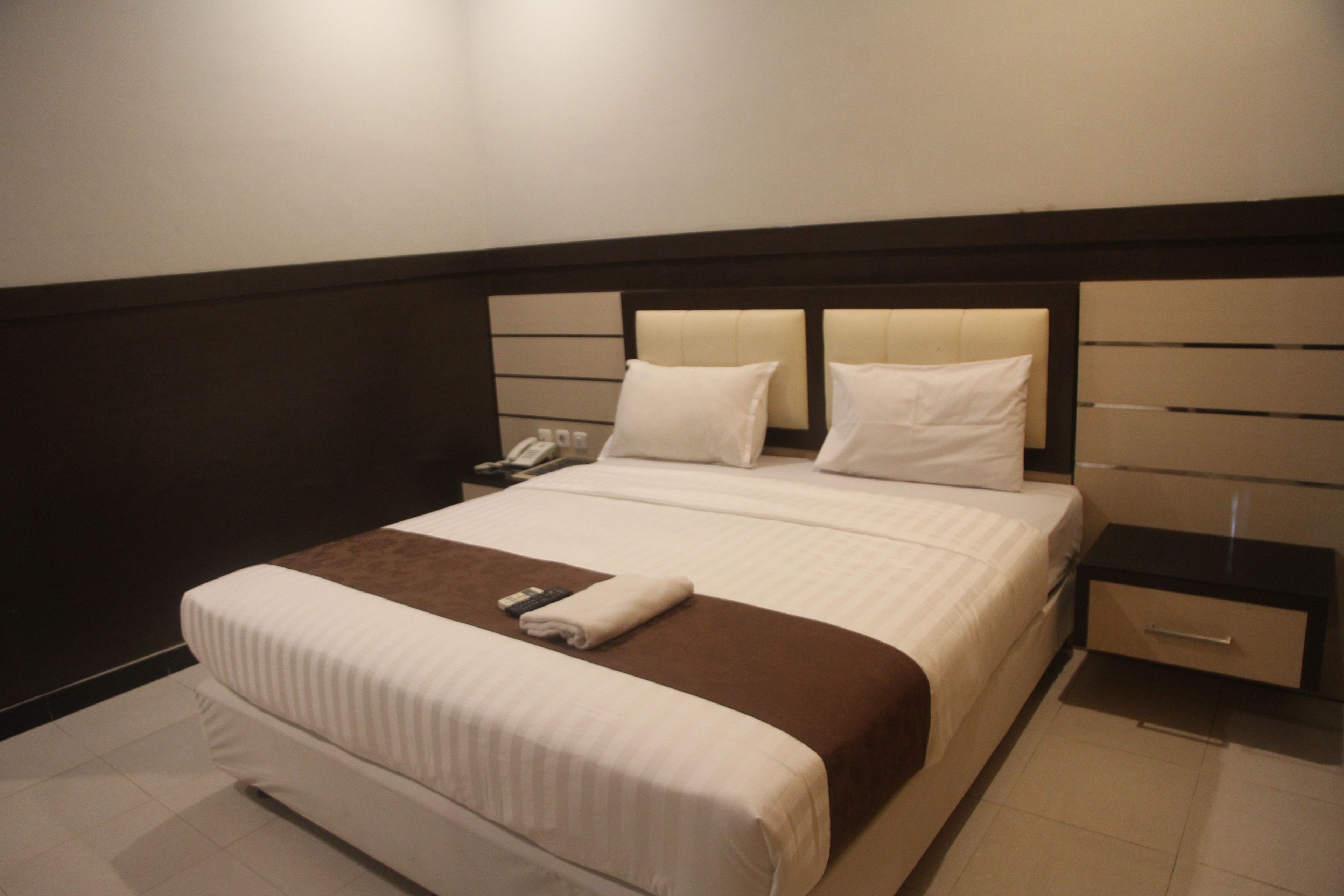 A hotel room with a large bed, a bedside table, a nightstand, and a wall-mounted phone.